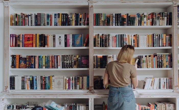 Woman standing in front of full bookshelf facing the books