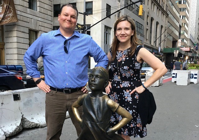 A man and women stand by the fearless girl statue
