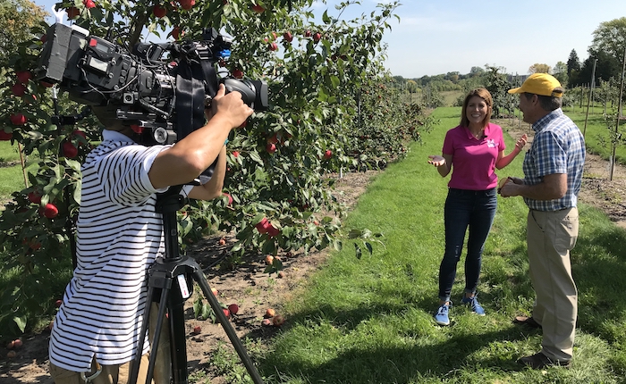 Person with camera records two people talking in an apple orchard