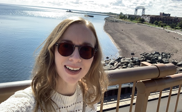 Woman takes a selfie in front of a harbor with the Duluth Liftbridge in the background