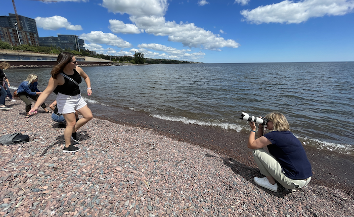 A woman takes a photo of another woman skipping rocks