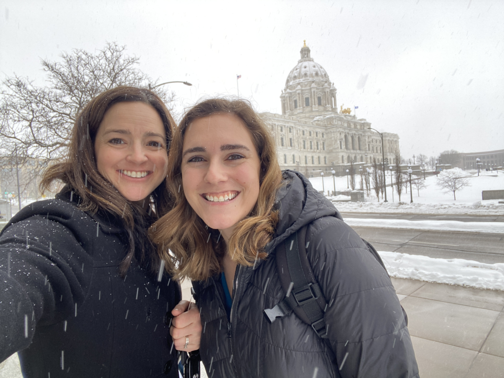 Two women take a selfie in the snow in front of the Minnesota state capitol.