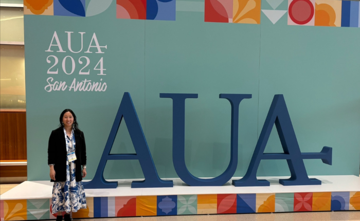 Hyedi Nelson stands in front of a branded sign at the American Urological Association Annual Meeting in San Antonio, Spring 2024.