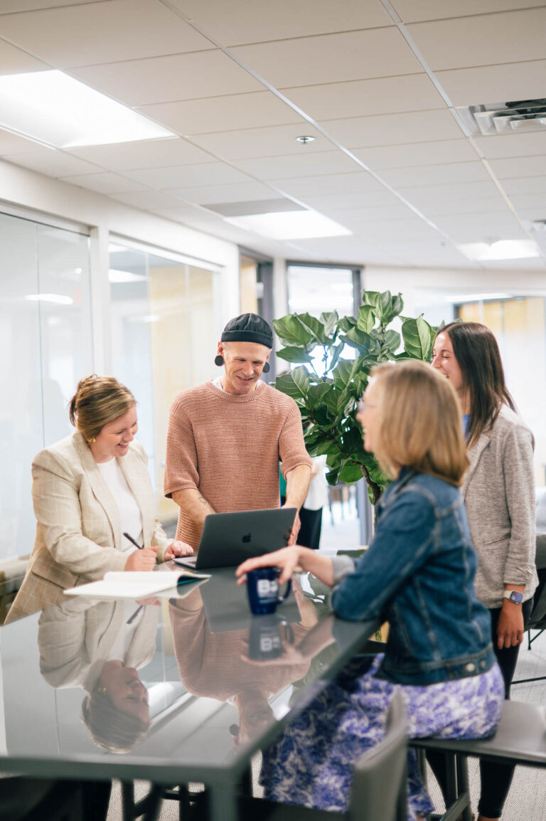 four smiling individuals surround a table in a work office